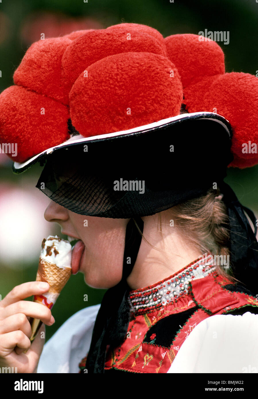 Une fille lèche la crème glacée lors d'un festival dans la Forêt Noire d'Allemagne, tout en portant un chapeau traditionnel avec des pompons rouge qui indique qu'elle n'est pas mariée. Banque D'Images