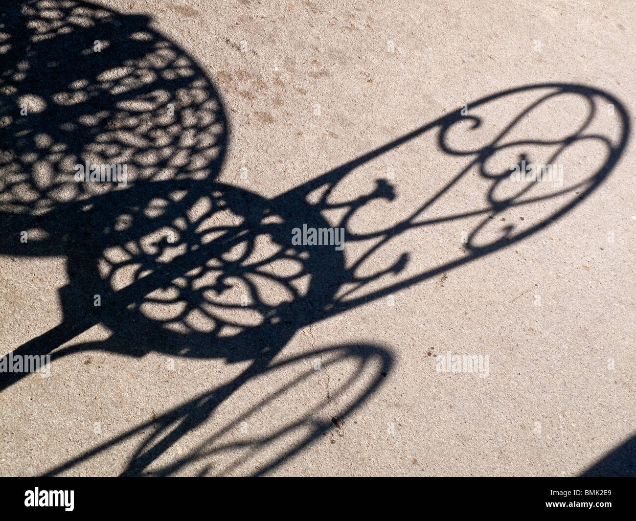 Ombre de métal ouvragé cafe chaise et table sur l'asphalte en plein soleil Banque D'Images