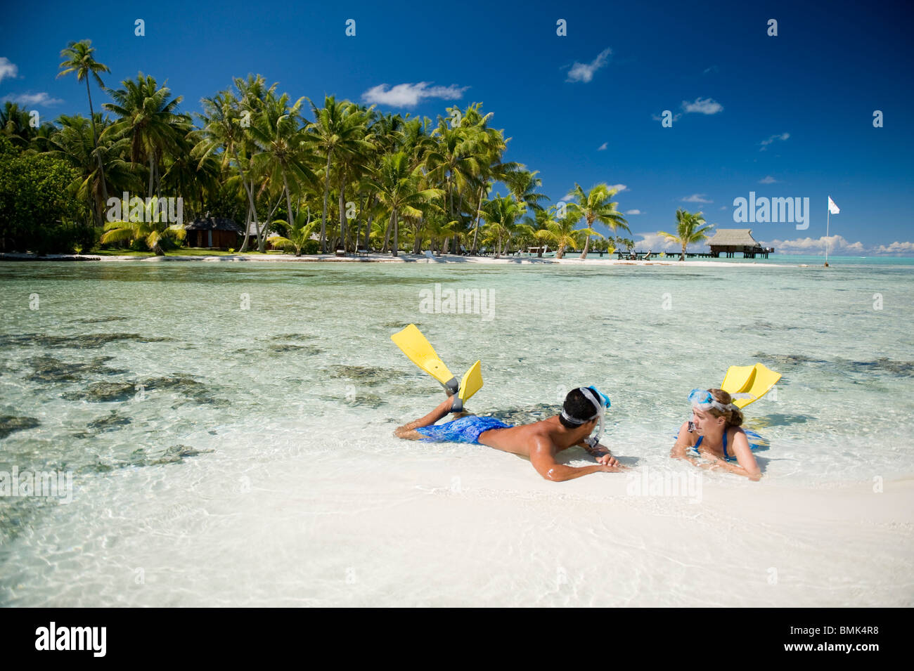 Un homme et une femme sur une plage d'un hôtel resort Tahiti avec matériel de plongée (palmes et masque). Ils sont en train de bronzer sur le sable. Banque D'Images