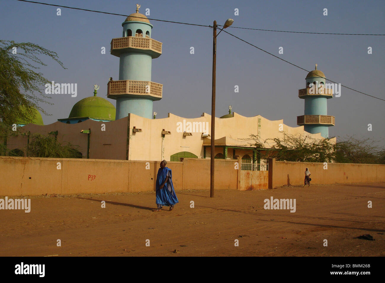 Homme portant une robe musulmane traditionnelle bleu, en passant par une mosquée et ses minarets vert Banque D'Images