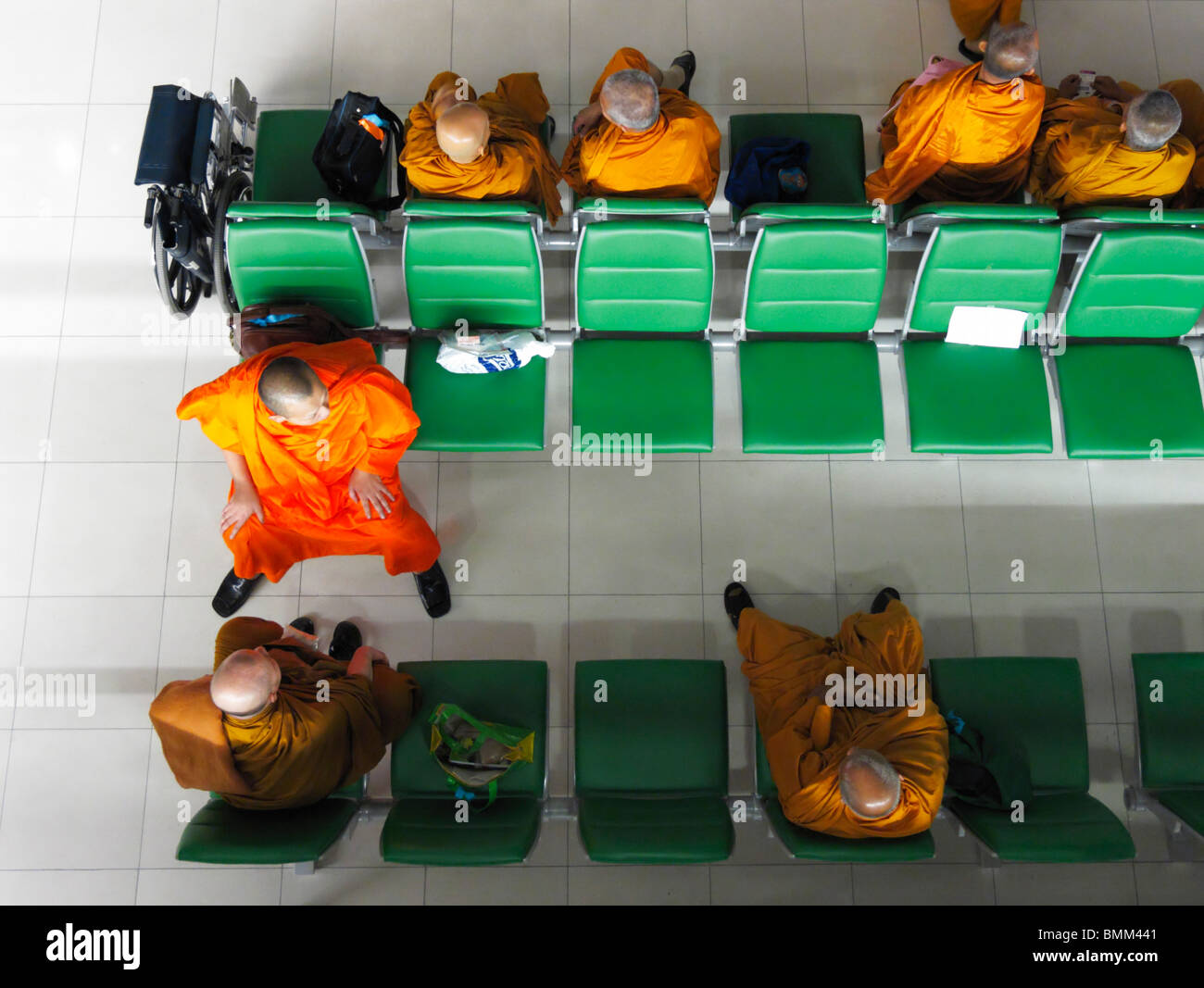 Un groupe de moines thaïlandais à revêtement orange assis sur des bancs verts attendant leur vol vers Zurich Kloten (ZRH/LSZH), Bangkok TH Banque D'Images