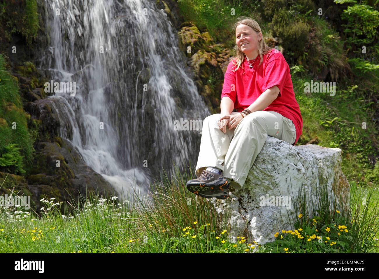 Jeune femme assise sur un rocher en face d'une cascade près de Donegal Ardara, Co., République d'Irlande Banque D'Images