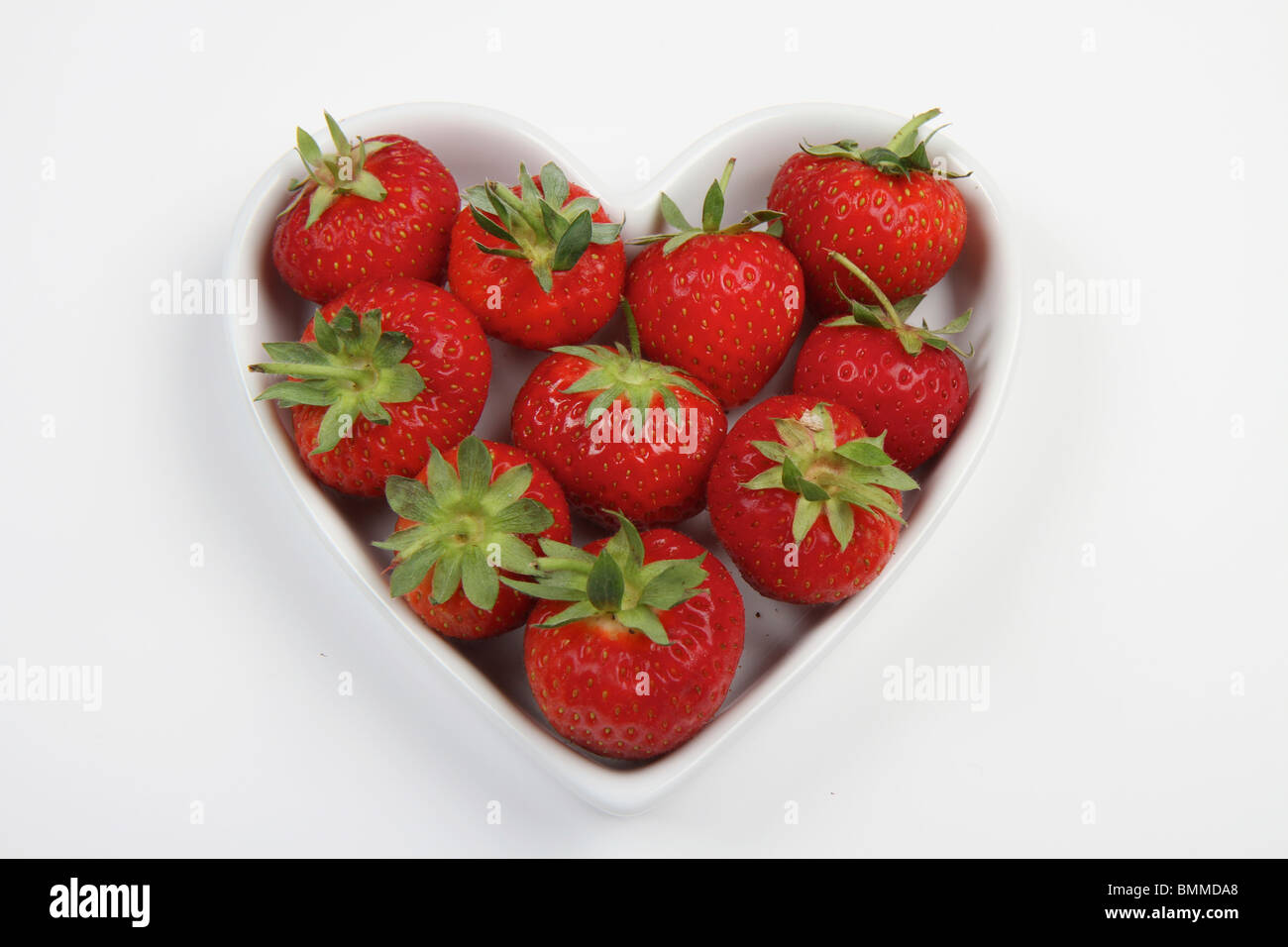 Rouge vibrant des fraises dans un plat en forme de coeur d'amour sur un fond blanc. Banque D'Images