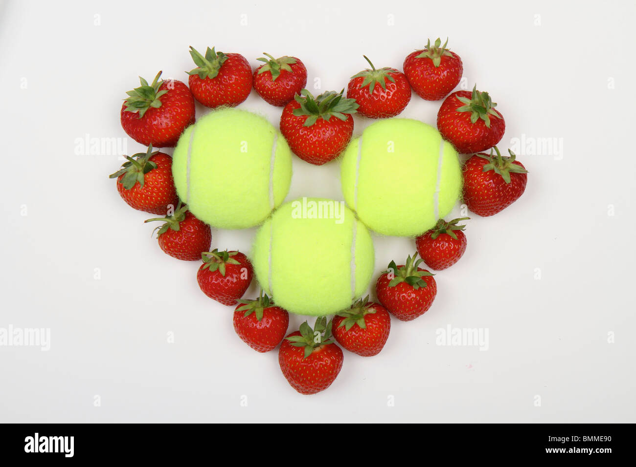 Fraises rouges en forme de coeur d'amour sur un fond blanc avec des balles de tennis dans le centre Banque D'Images