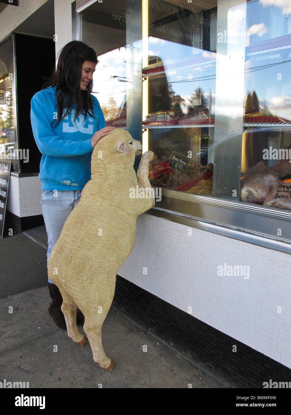 Une jeune fille avec un gimmick de vente promotionnelle humoristique d'un mouton modèle regardant dans la fenêtre d'un boucher Banque D'Images