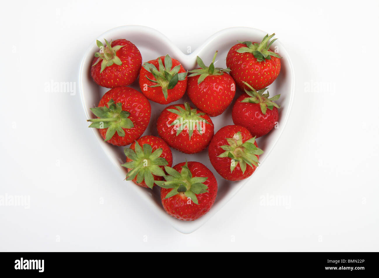 Rouge vibrant des fraises dans un plat en forme de coeur d'amour sur un fond blanc. Banque D'Images