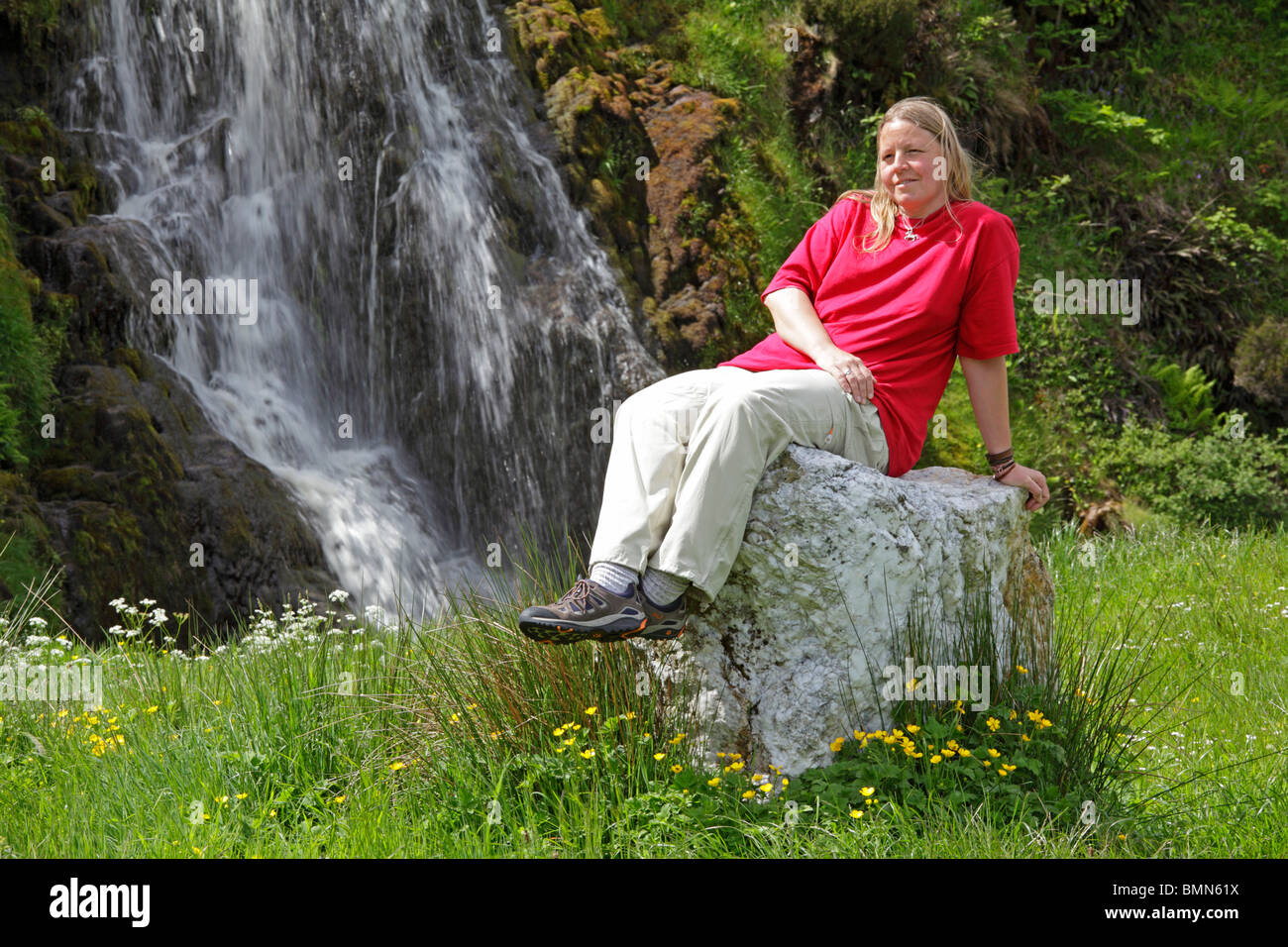 Jeune femme assise sur un rocher en face d'une cascade près de Donegal Ardara, Co., République d'Irlande Banque D'Images