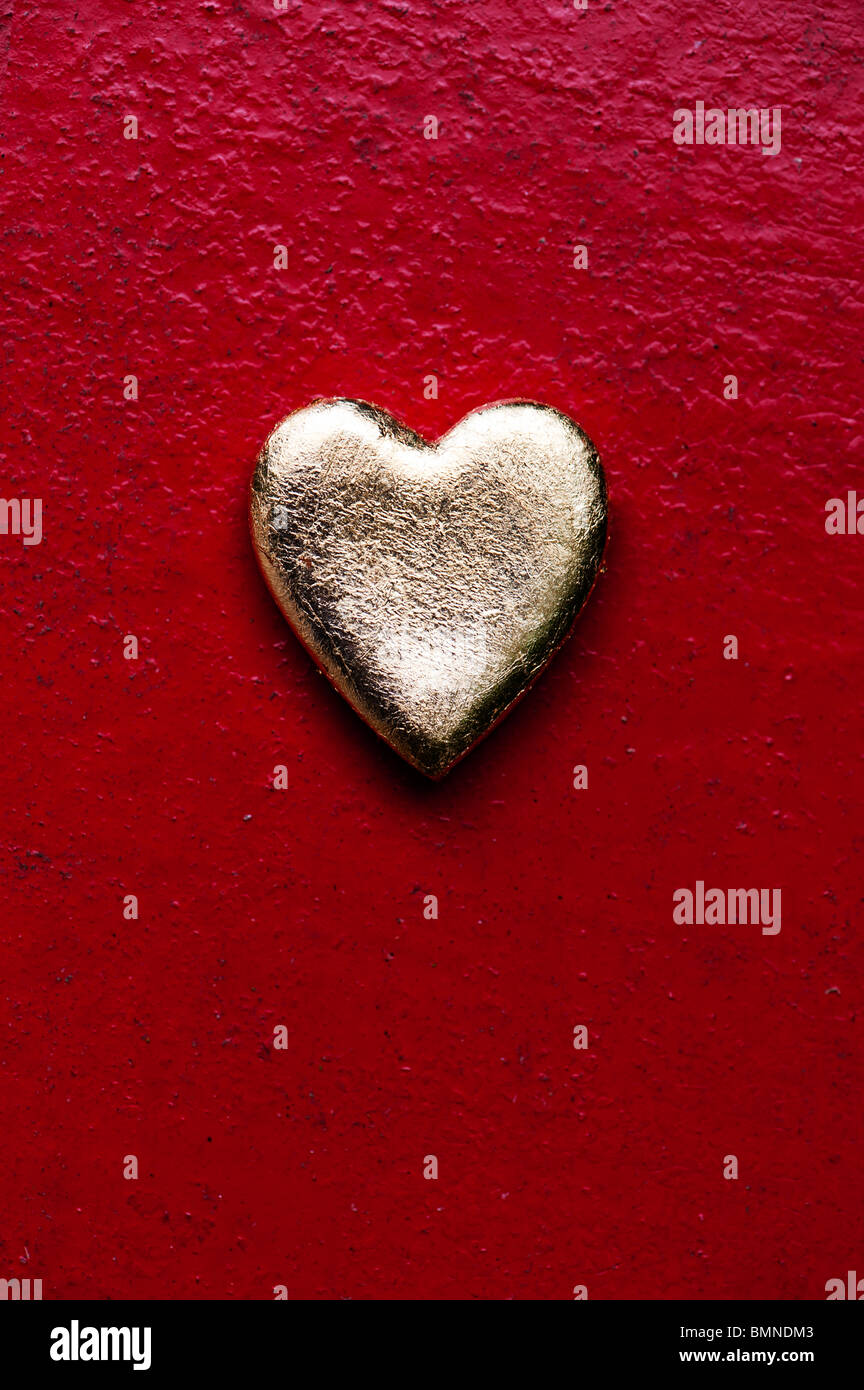 Forme de coeur en or contre texture rouge metal fond peint Banque D'Images