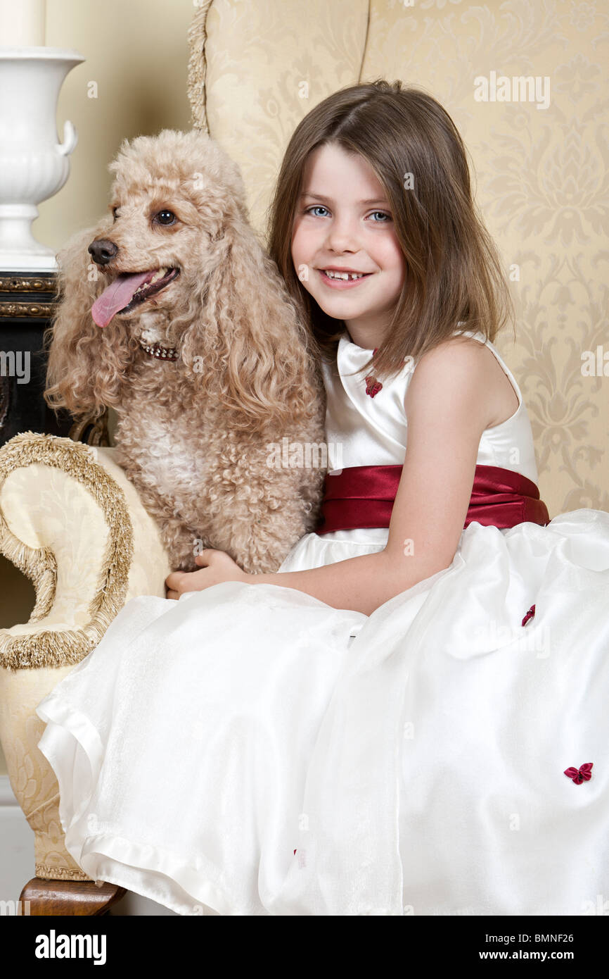 Tourné d'une heureuse fille blonde dans un grand fauteuil avec un abricot caniche miniature Française Banque D'Images