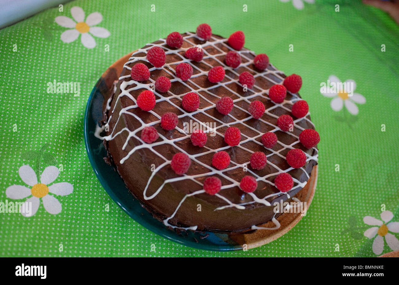 Un gâteau au chocolat avec des framboises est situé sur une nappe colorée. Banque D'Images