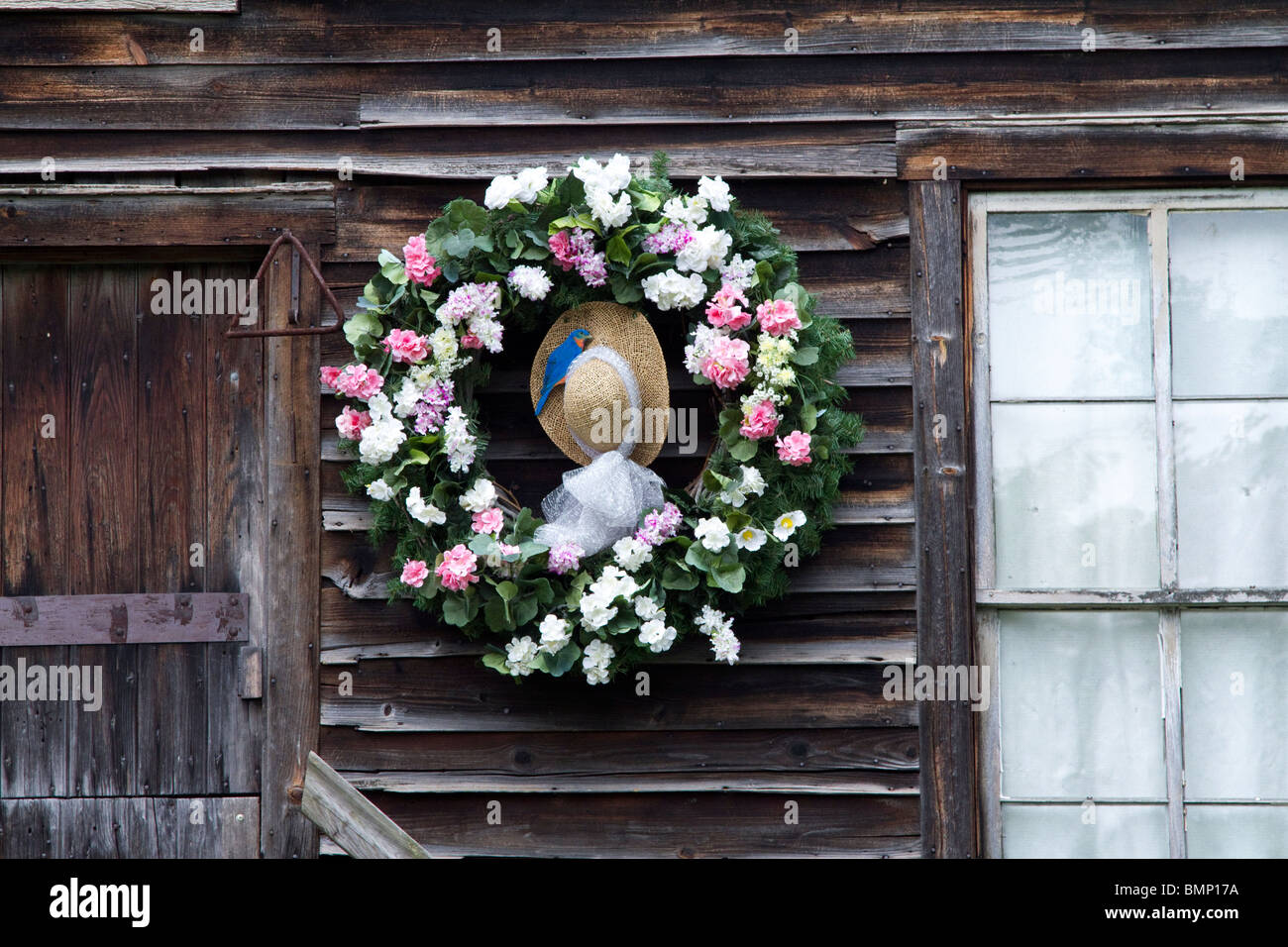 Une couronne de printemps avec un chapeau au centre accroché sur un ancien moulin à eau en bois patiné Banque D'Images