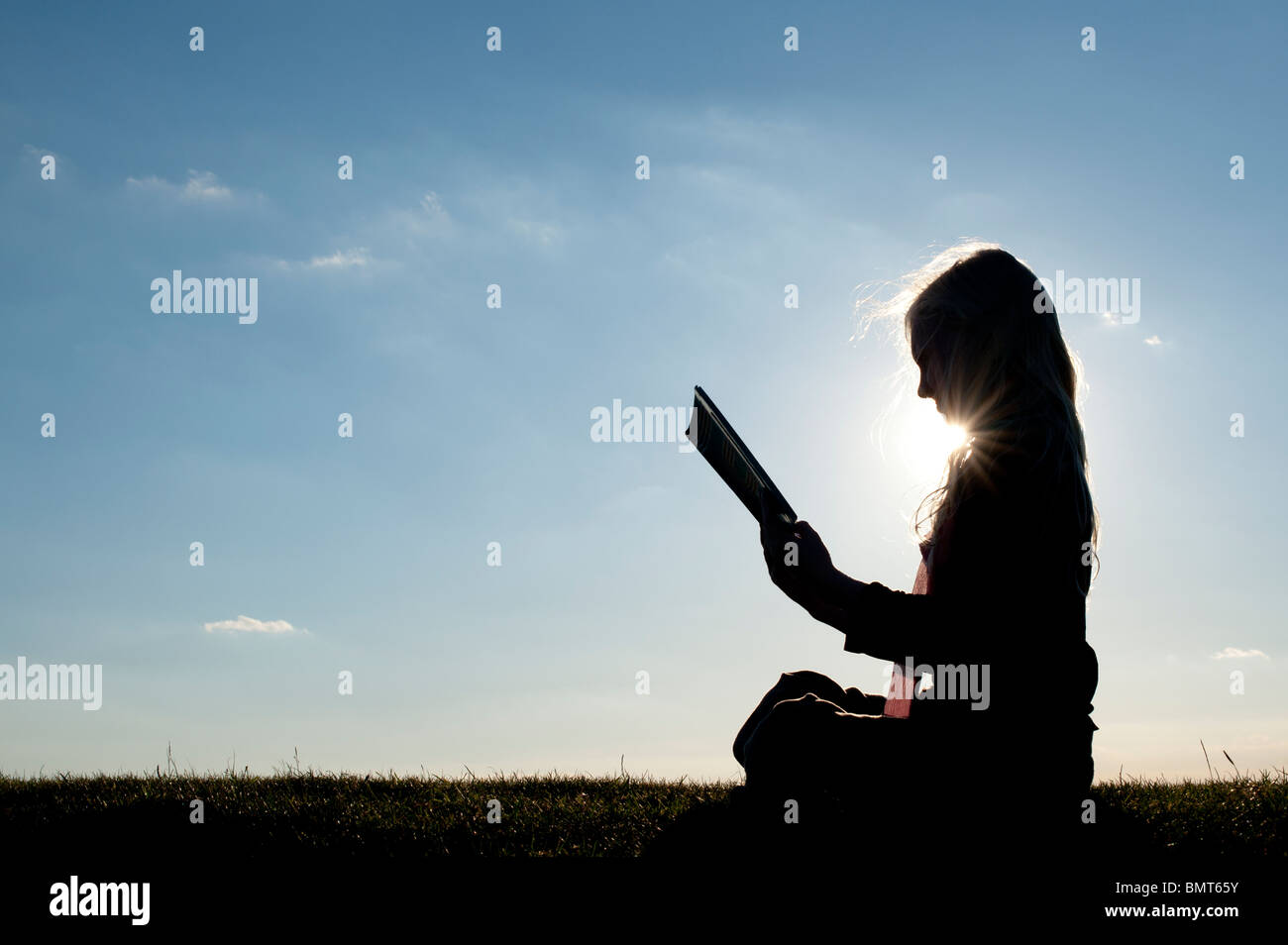 Jeune fille s'asseoir pour lire un livre au coucher du soleil. Silhouette Banque D'Images