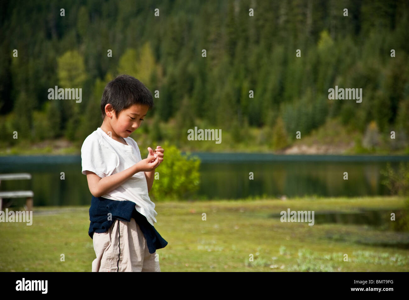 Un garçon asiatique regarde un champignon dans sa main à l'extérieur par un lac Banque D'Images