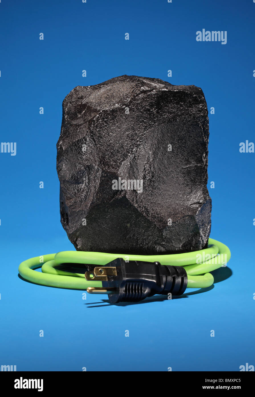 Un grand morceau de charbon noir avec une rallonge électrique vert et bouchon rétractable autour sur un fond bleu lumineux. Banque D'Images