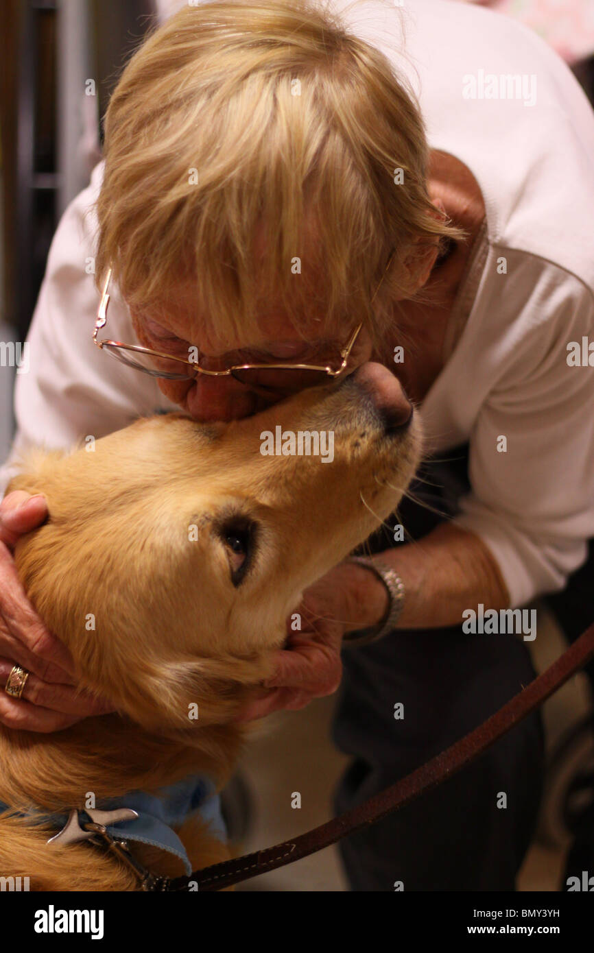 Senior citizen embrassant un chien de thérapie au cours d'une visite Banque D'Images