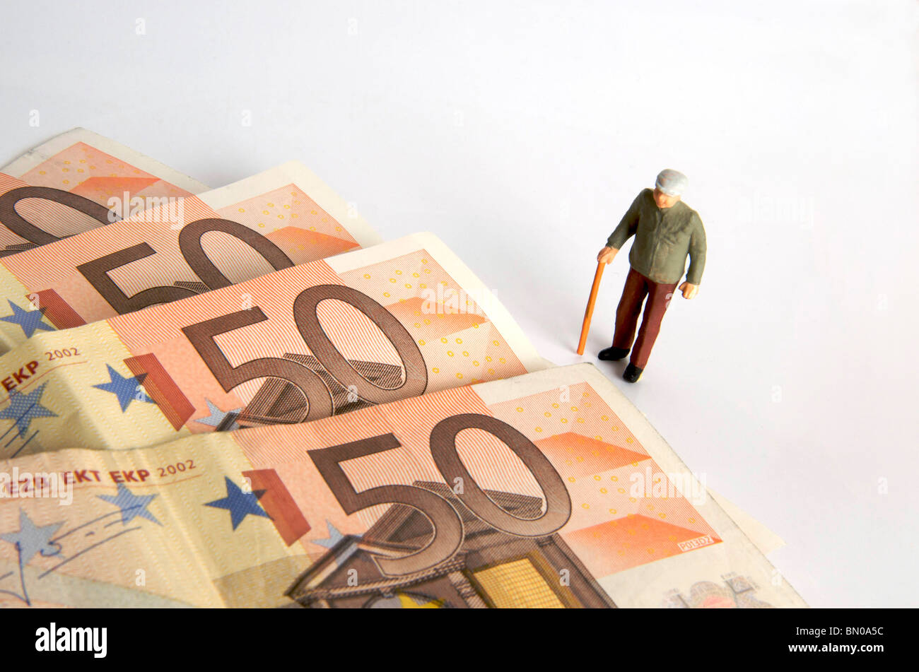 Petite figurine d'une personne âgée debout à côté de gros billets en euros sur un fond Uni Banque D'Images