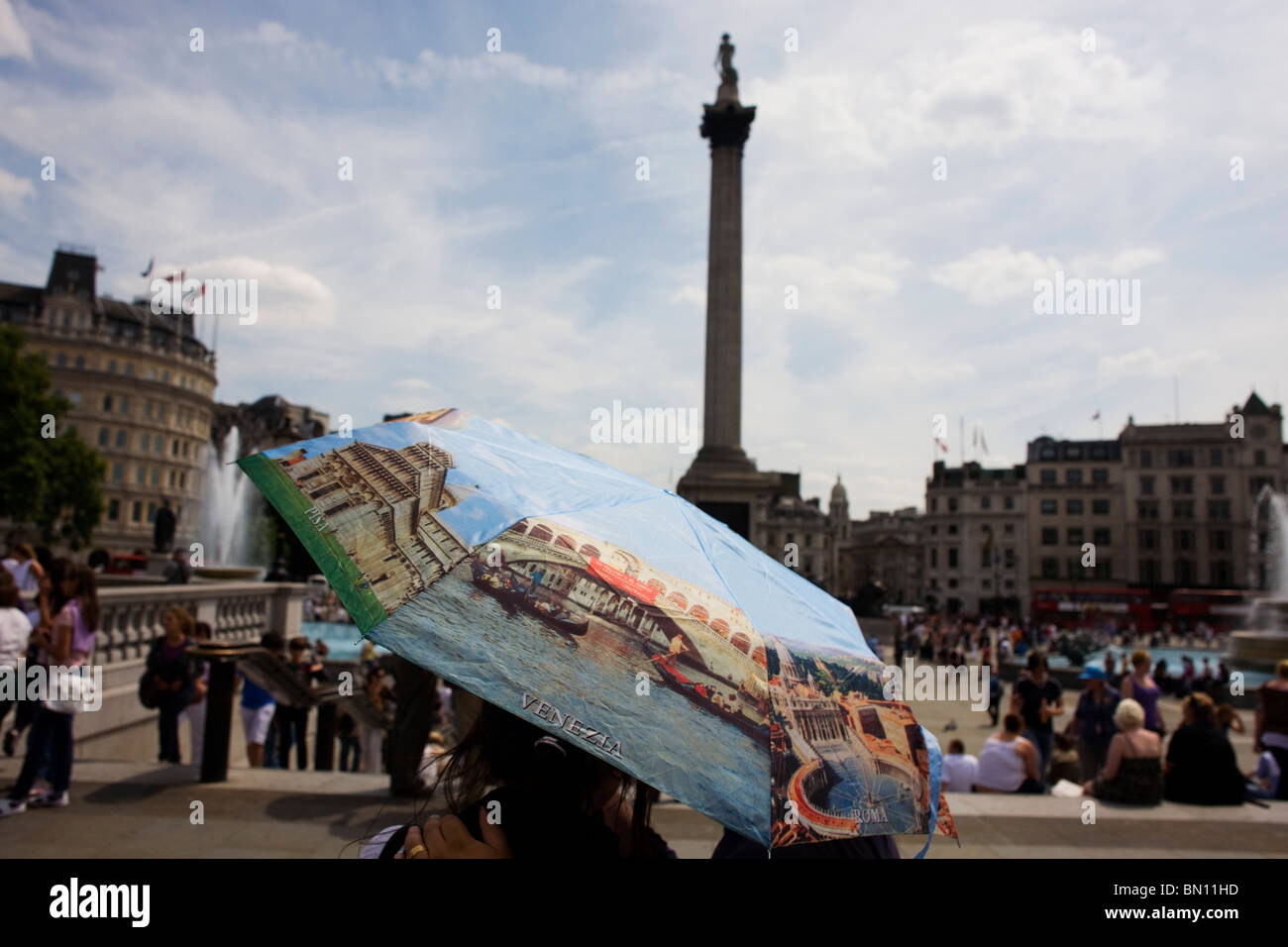 Un couple romantique stand in London's Trafalgar Square sous un parapluie avec des photos de villes italiennes. Banque D'Images