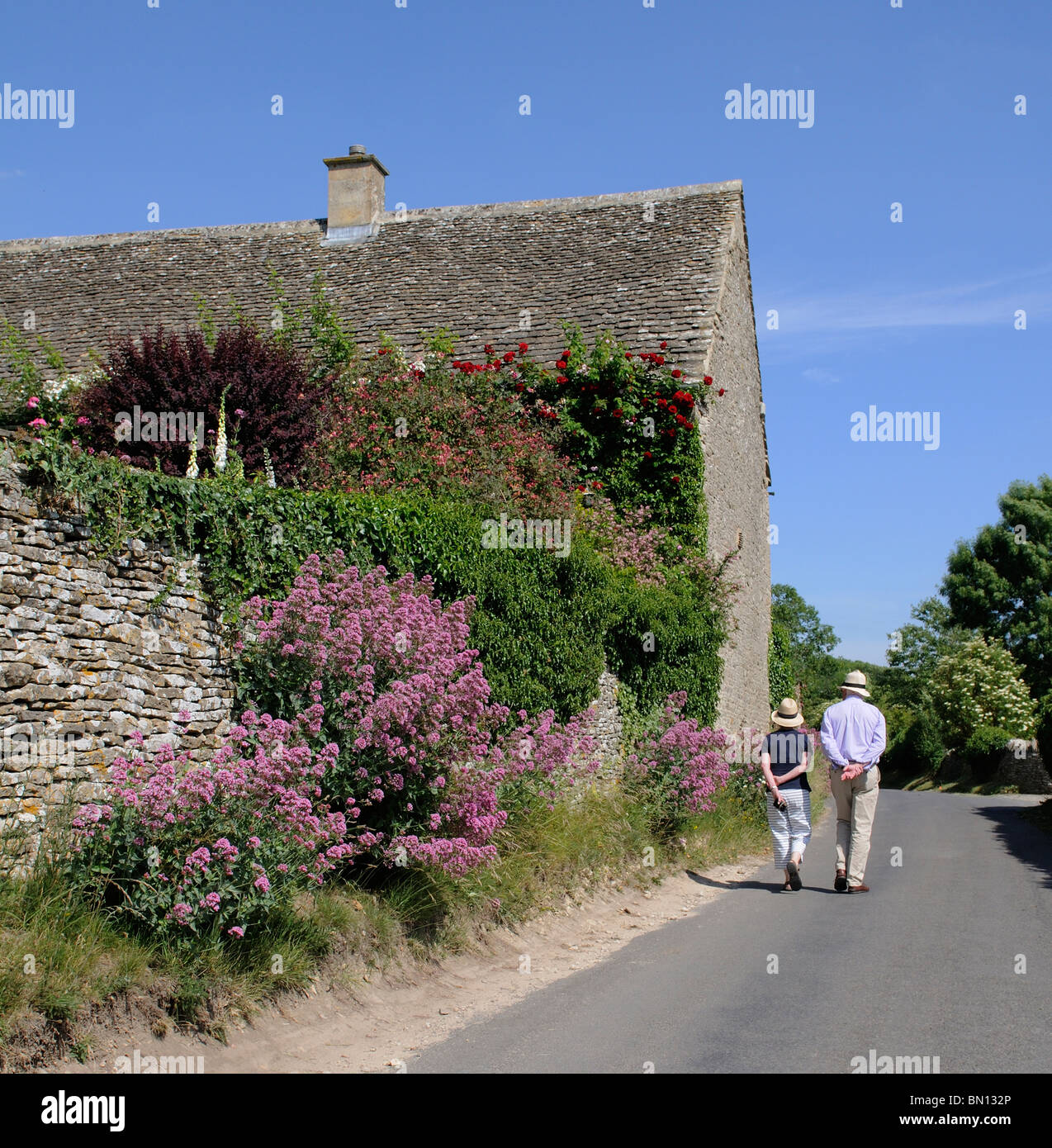 Couple en train de marcher le long d'un chemin de campagne dans les Cotswolds England UK muret de pierres sèches fleurs Banque D'Images