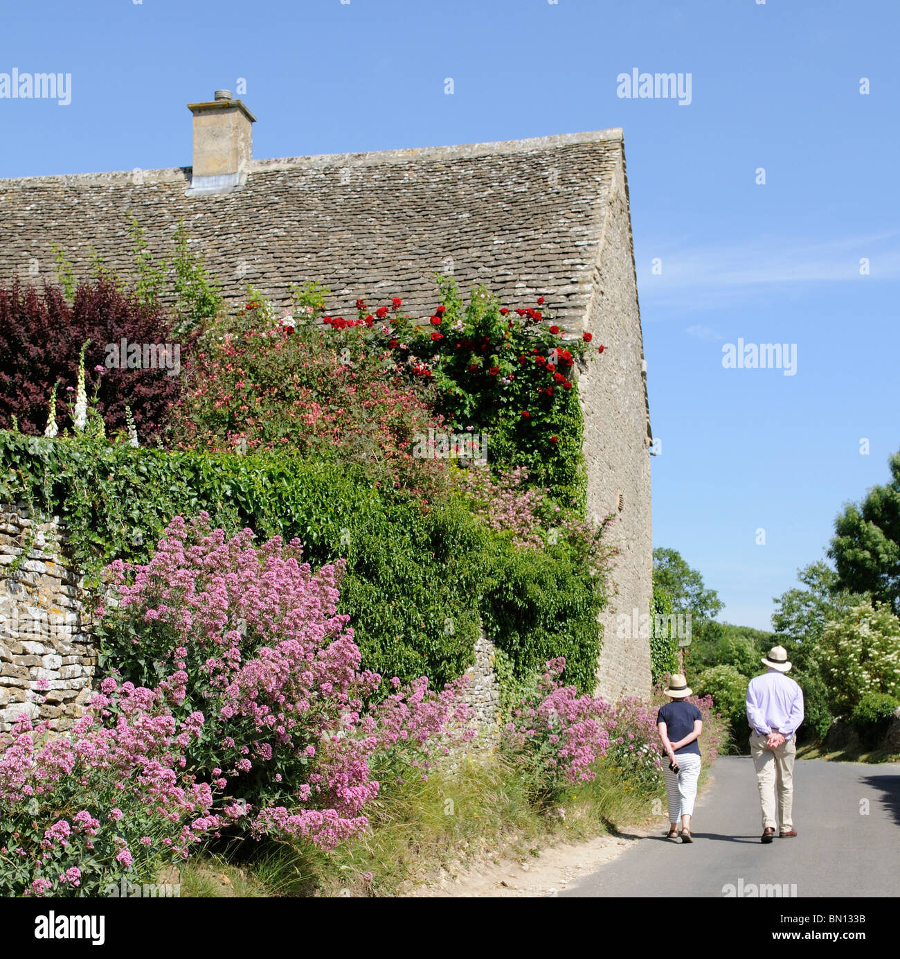 Couple en train de marcher le long d'un chemin de campagne dans les Cotswolds England UK muret de pierres sèches fleurs Banque D'Images