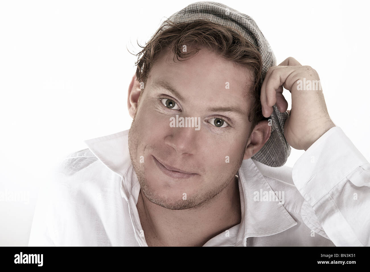 Jeune homme en chemise blanche avec capuchon plat smiling at camera, portrait Banque D'Images