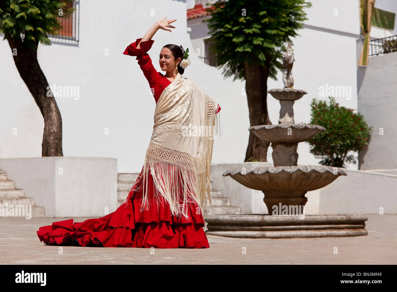 Danseuse de flamenco espagnol traditionnel femme dansant dans une robe rouge et crème châle dancing in a town square avec une fontaine en pierre Banque D'Images