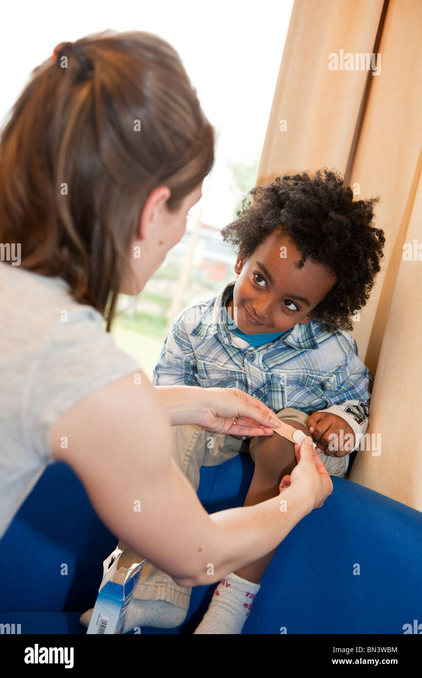 Enseignant de maternelle l'application d'un plâtre sur jambe garçons Banque D'Images