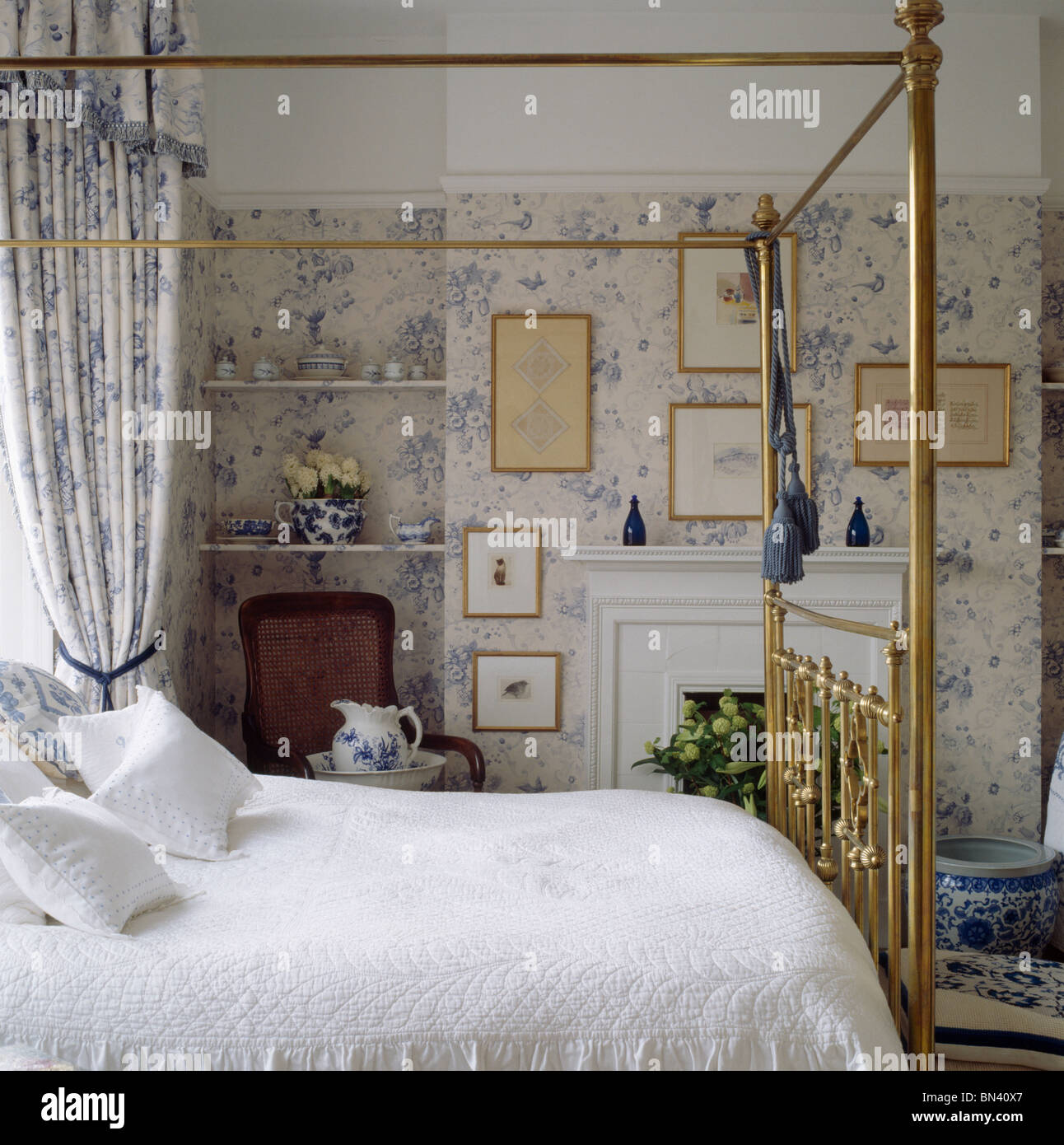 Couette blanche sur laiton lit avec rideaux à motifs floraux bleus dans la chambre avec un papier peint fleuri blanc +bleu Banque D'Images