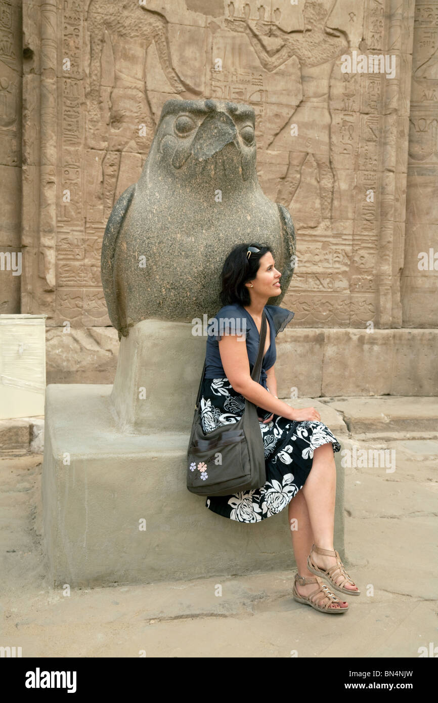 Une femme assise touristique d'une statue de l'ancien dieu égyptien Horus dans le parvis du Temple d'Edfou, Egypte Banque D'Images
