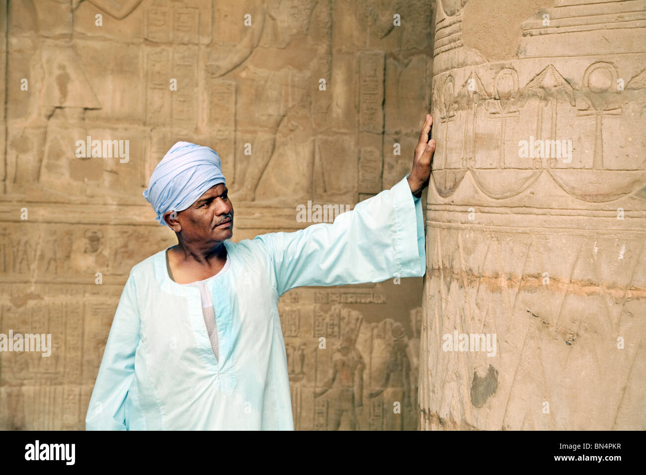 Un homme portant un guide égyptien galabia bleu appuyé contre une colonne, le temple d'Hatshepsout, Luxor, Égypte Banque D'Images