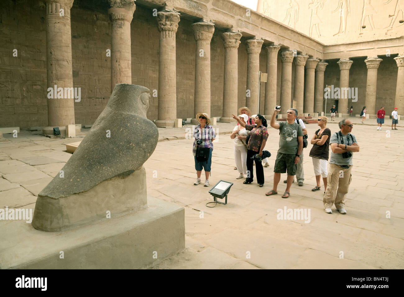 Un groupe de touristes sur une visite guidée d'examiner une statue d'Horus, l'avant-cour, temple d'Edfou, Edfou, Egypte Banque D'Images