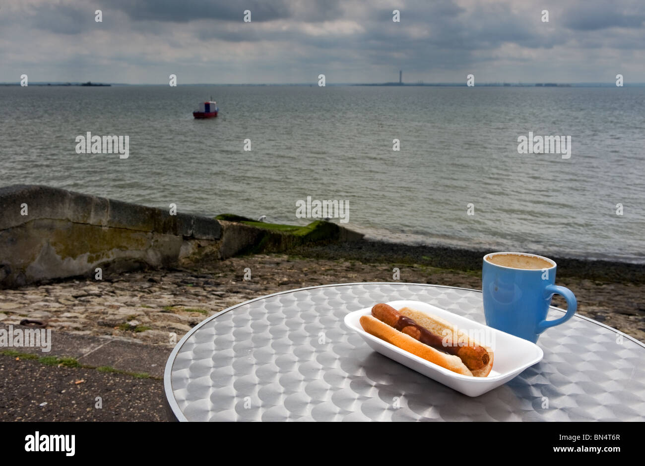 Un hot-dog et une tasse de café sur une table à Southend on sea dans l'Essex. Banque D'Images