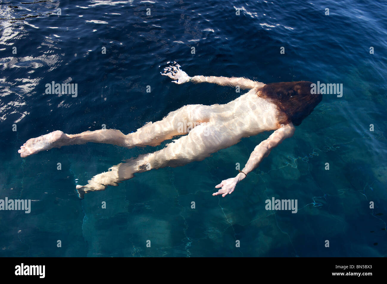 Femme nue (20 - 35) Nager dans une mare sombre. Banque D'Images