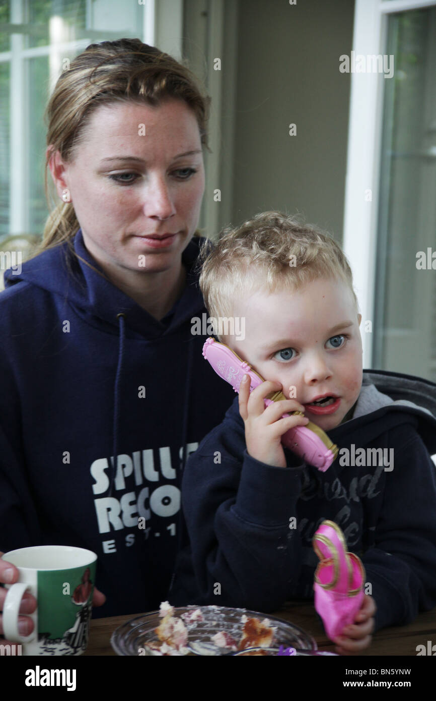 Tout-petit garçon assis avec sa maman avec un modèle de téléphone mobile jouet semblant libéré Banque D'Images