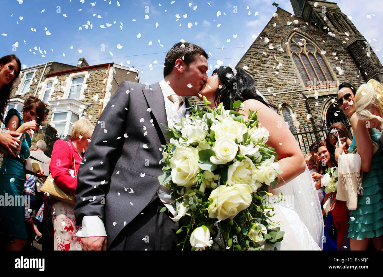 Bride and Groom kissing sous les confettis lancés par les invités du mariage à l'extérieur d'une église sur leur grand jour mariage spécial Banque D'Images