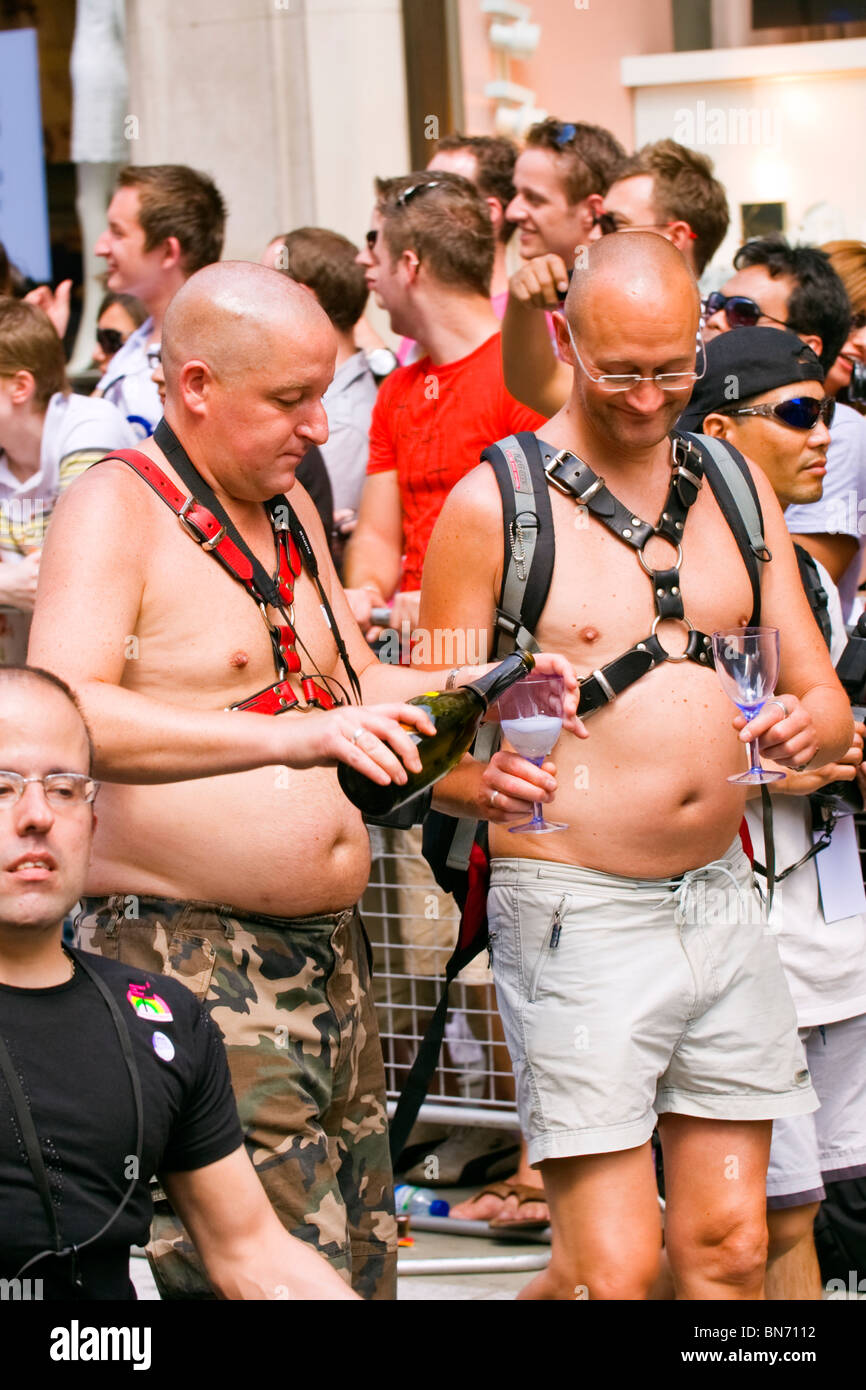 Londres Gay Pride Parade , deux jeunes hommes chauve , couple , en shorts  avec paunches & cuir S&M bondage gear drinking champagne Photo Stock - Alamy