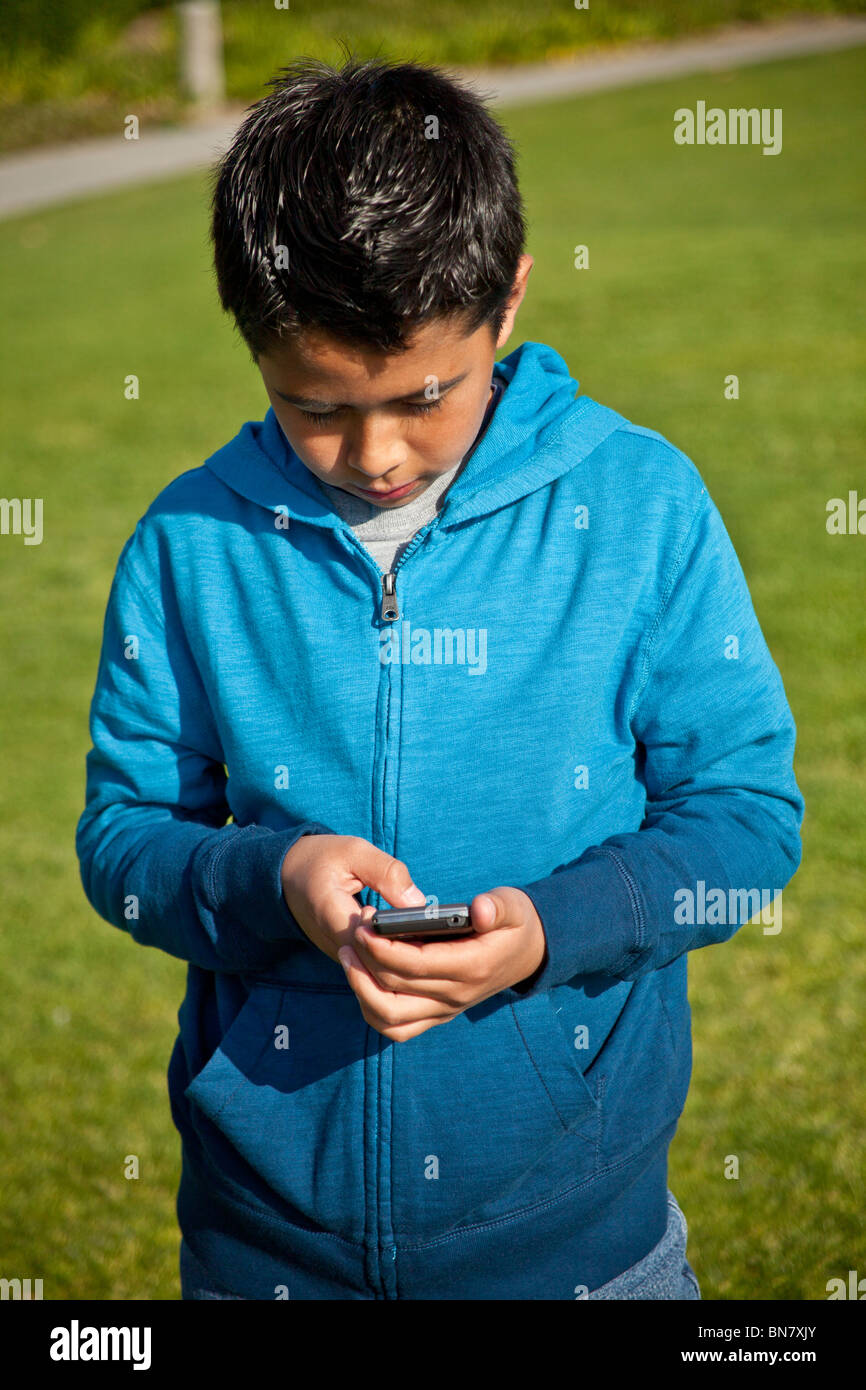 9 -11 ans garçon Hispanique à l'aide d'iPhone sms sur téléphone mobile. M. © Myrleen Pearson Banque D'Images