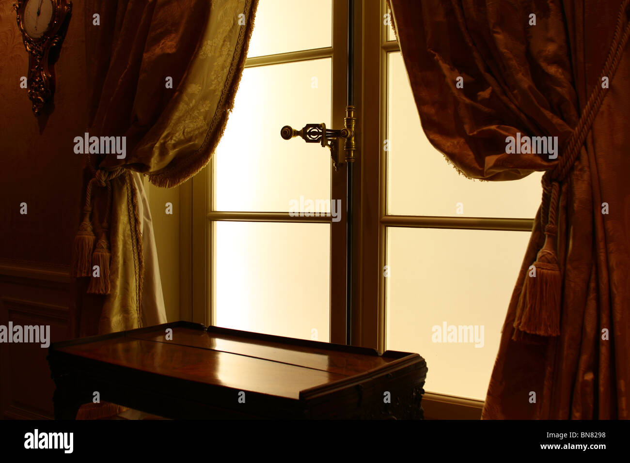 Lumière tamisée sur cadre jaune avec fenêtre en verre fumé table console entre les rideaux or jaune noué sur glands. Banque D'Images