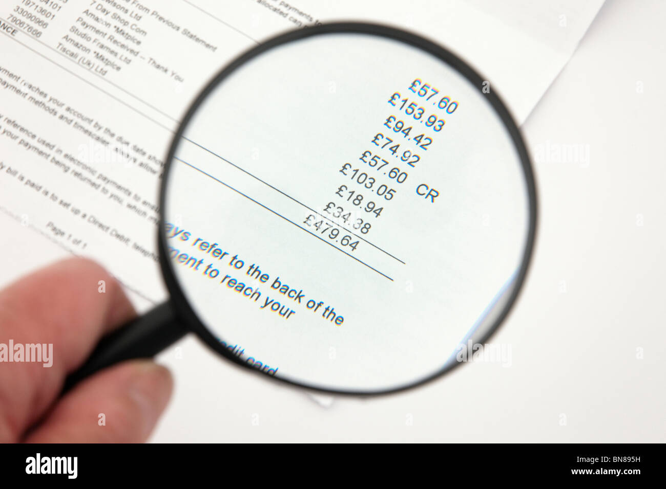 Personne titulaire d'une loupe pour examiner une grande carte de crédit. Banque D'Images