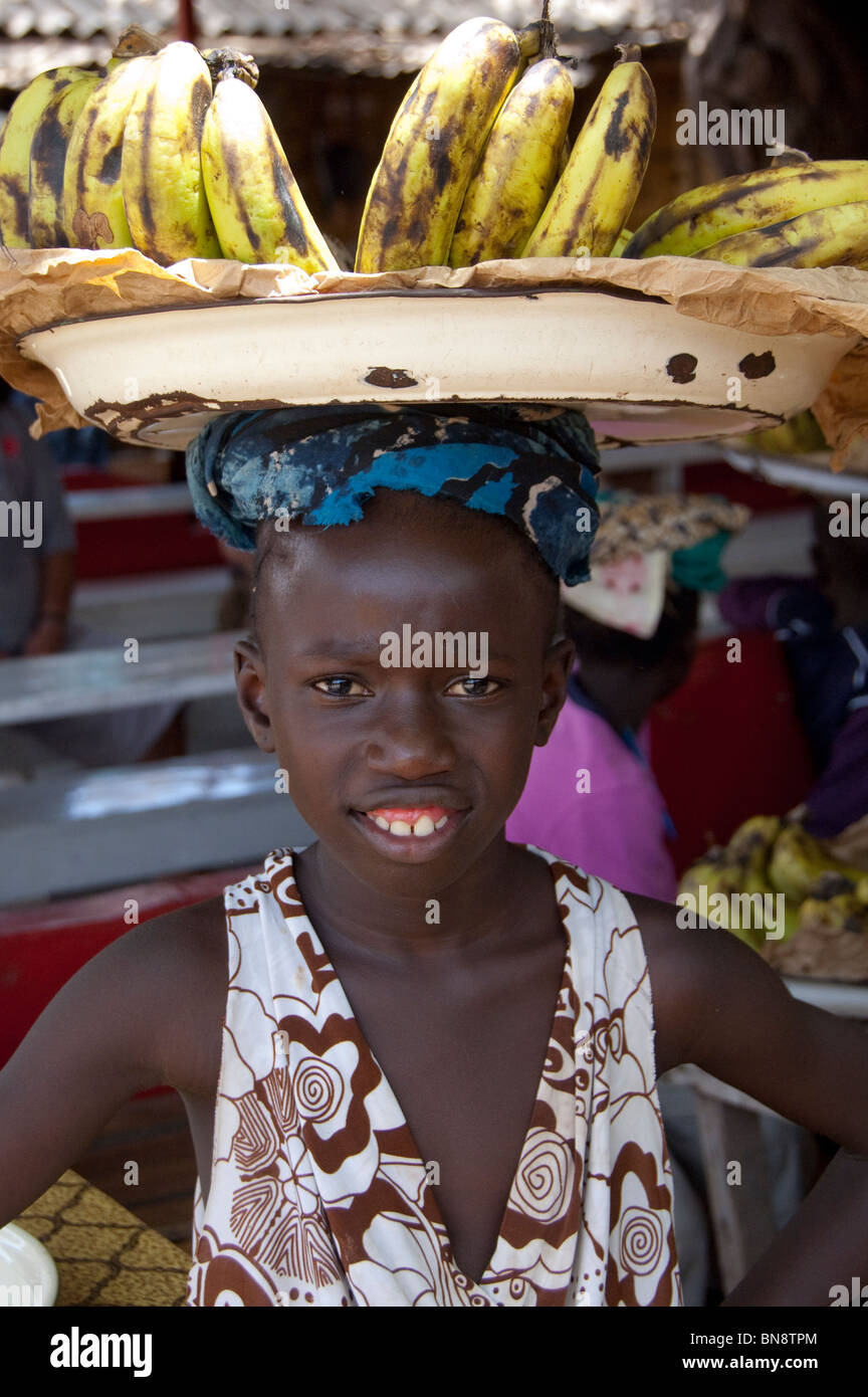L'Afrique, Gambie. Capitale de Banjul. Albert & Marché Marché artisanal de Banjul. Jeune vendeur de bananes avec des fruits sur la tête. Banque D'Images