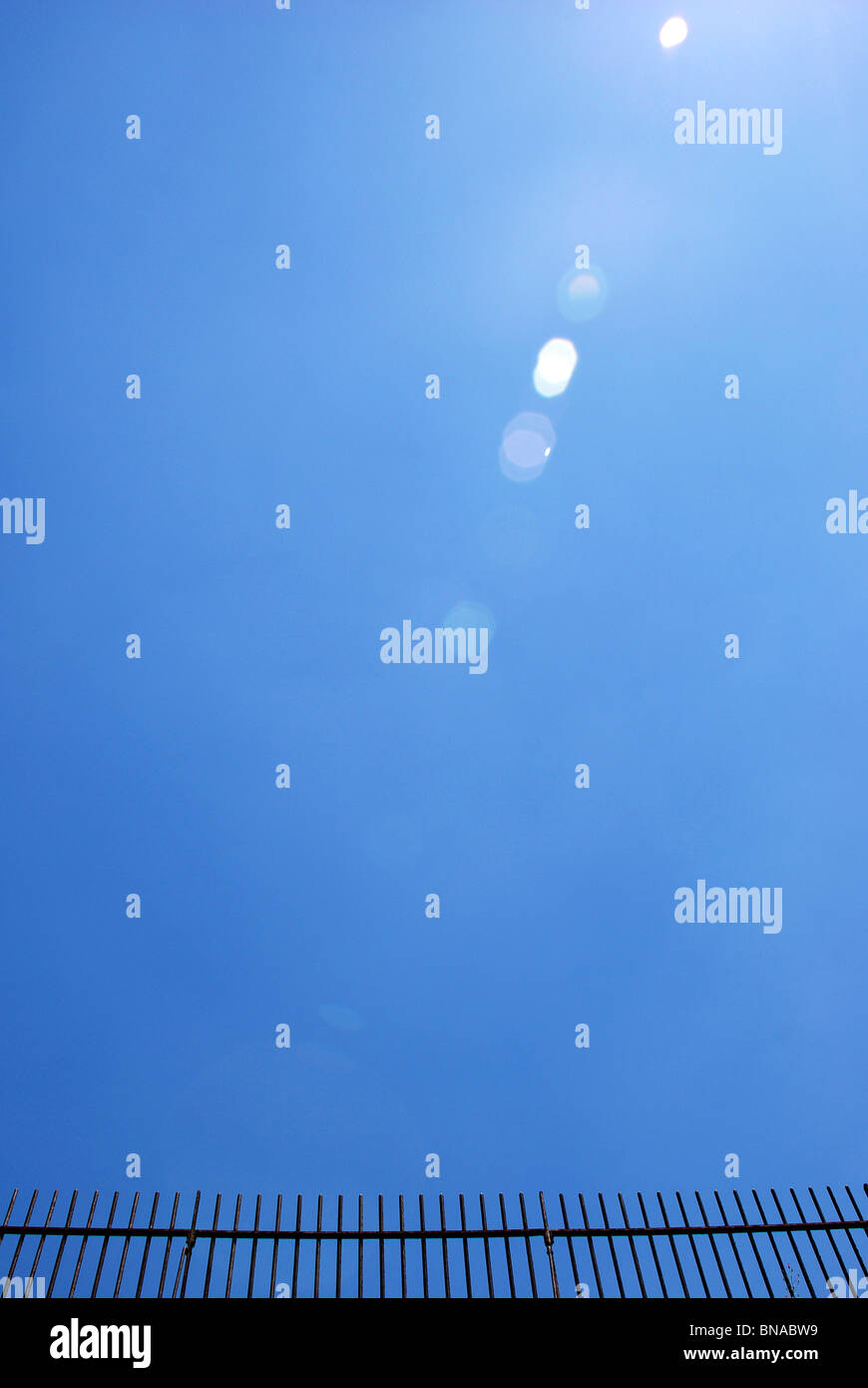 Clôture en fer forgé, contre un ciel bleu sans nuages, avec des reflets Banque D'Images Clôture en fer forgé, contre un ciel bleu sans nuages, avec des reflets Banque D'Images