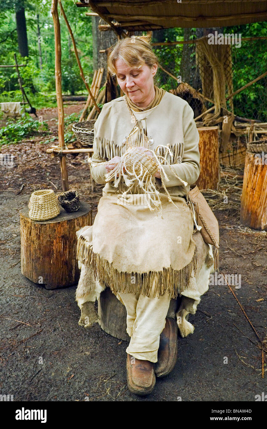 Un interprète vêtu comme un Indien Powhatan tisse un panier de paille pour montrer aux visiteurs la vie dans le début des années 1600, à Jamestown Settlement, New York, USA. Banque D'Images