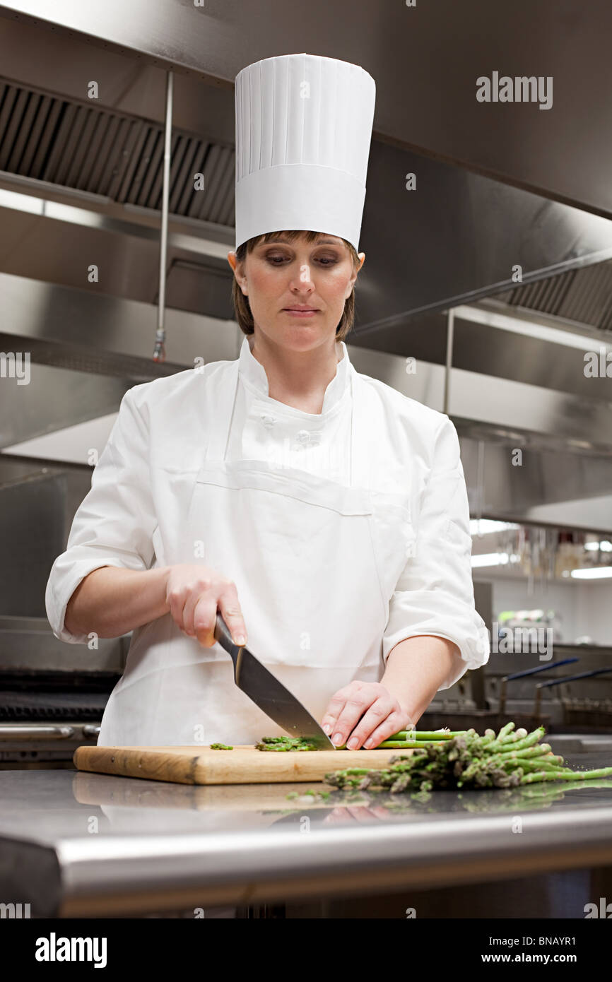 Femme chef chopping asperges dans cuisine commerciale Banque D'Images
