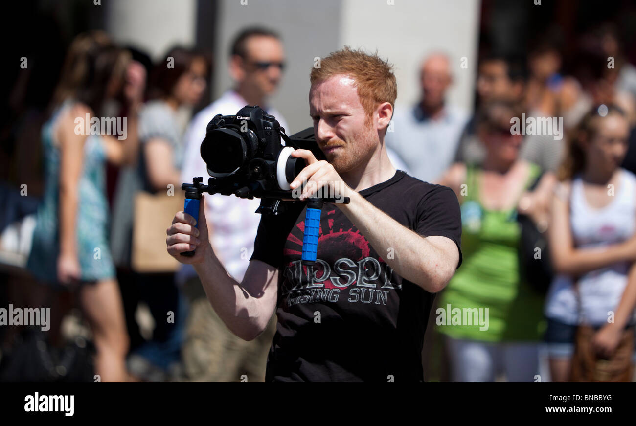 Vidéographe tournage avec un appareil photo reflex numérique, monté sur une plate-forme de soutien de l'épaule, London, England, UK Banque D'Images