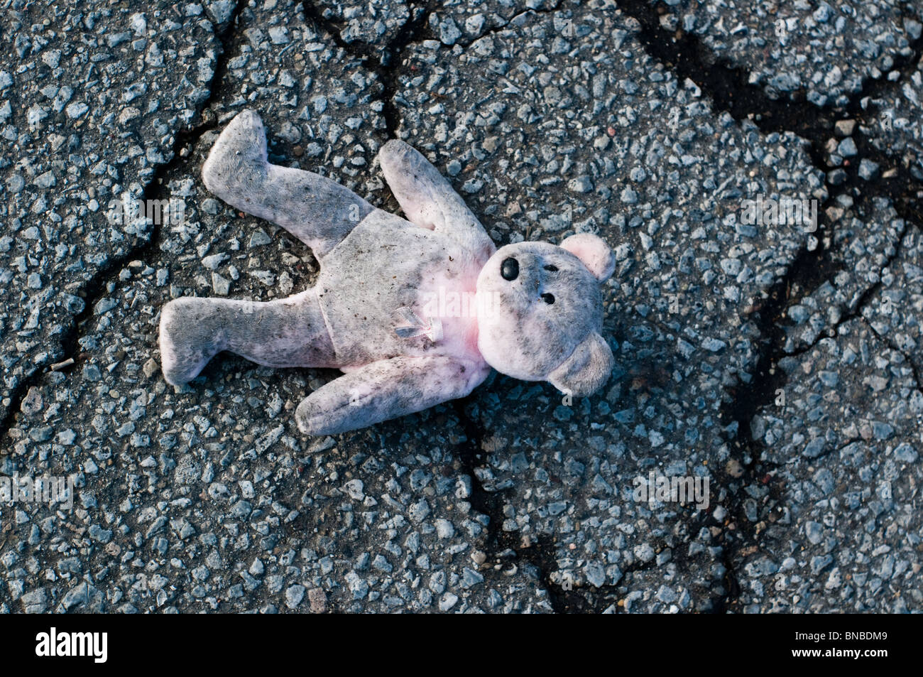 Un ours en peluche rose se trouve abandonné et sale sur le bord de la route. Banque D'Images