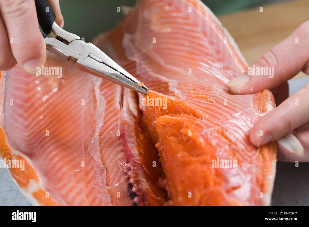 Personne à l'aide d'une pince pour retirer les os hors de filet de saumon. Banque D'Images