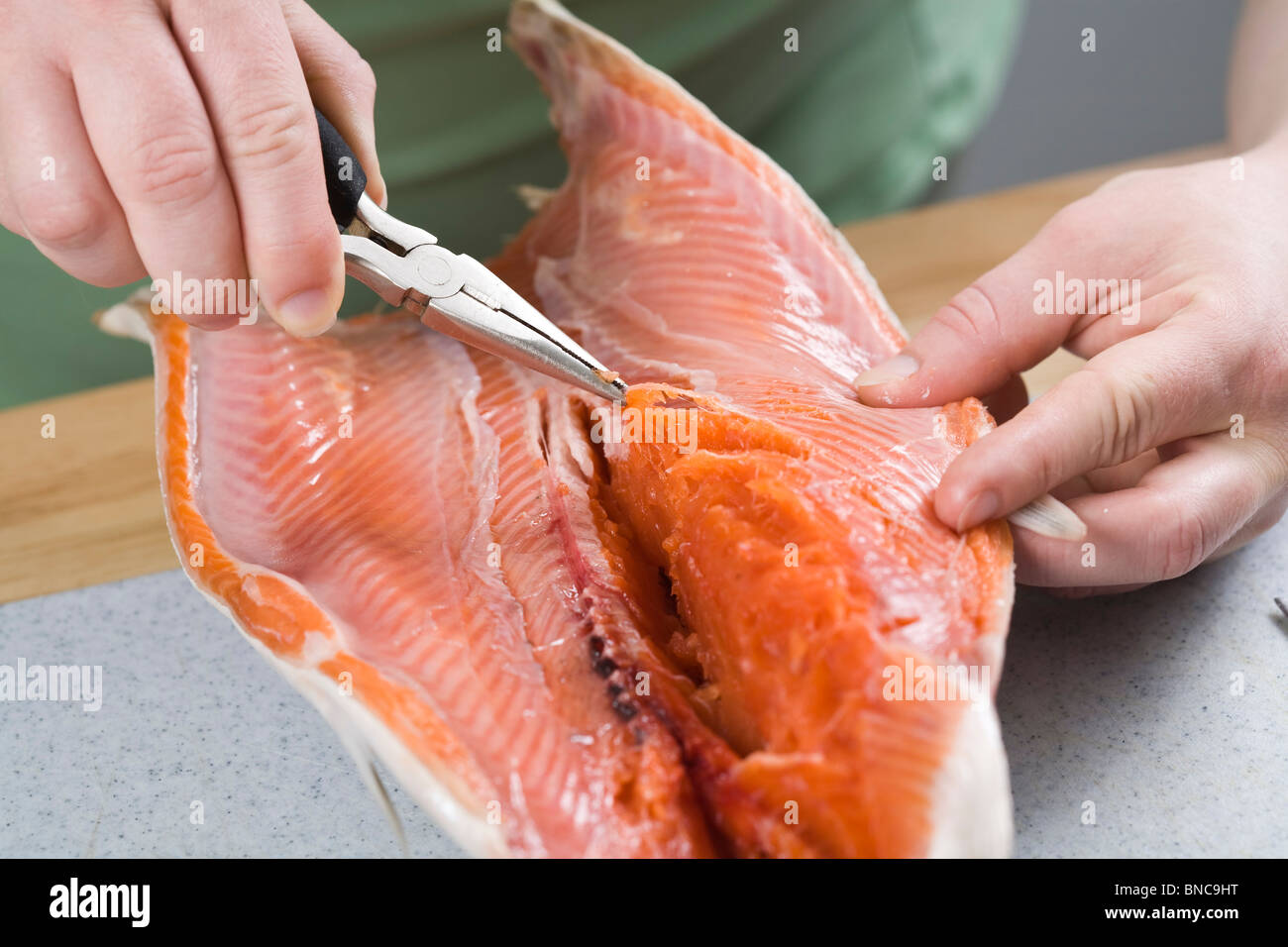 Personne à l'aide d'une pince pour retirer les os hors de filet de saumon. Banque D'Images