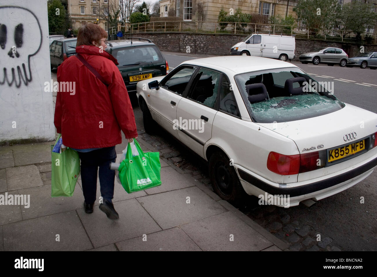 Woman with shopping bags oeil voiture vandalisée avec brisé des fenêtres, Bristol, Royaume-Uni Banque D'Images