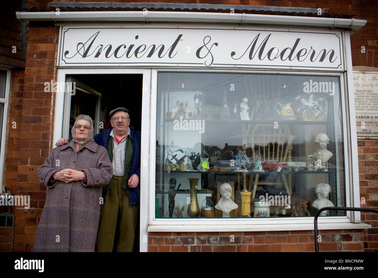 Couple de personnes âgées en dehors de leur boutique de seconde main et d'antiquités, Melton Mowbray, UK. Banque D'Images