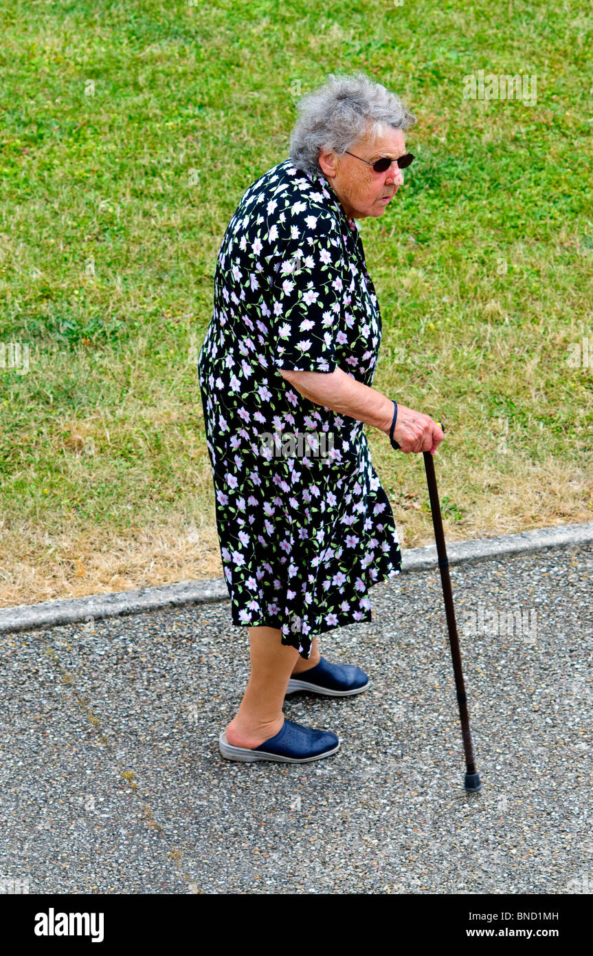 Femme âgée avec bâton de marche marche le long trottoir - France. Banque D'Images