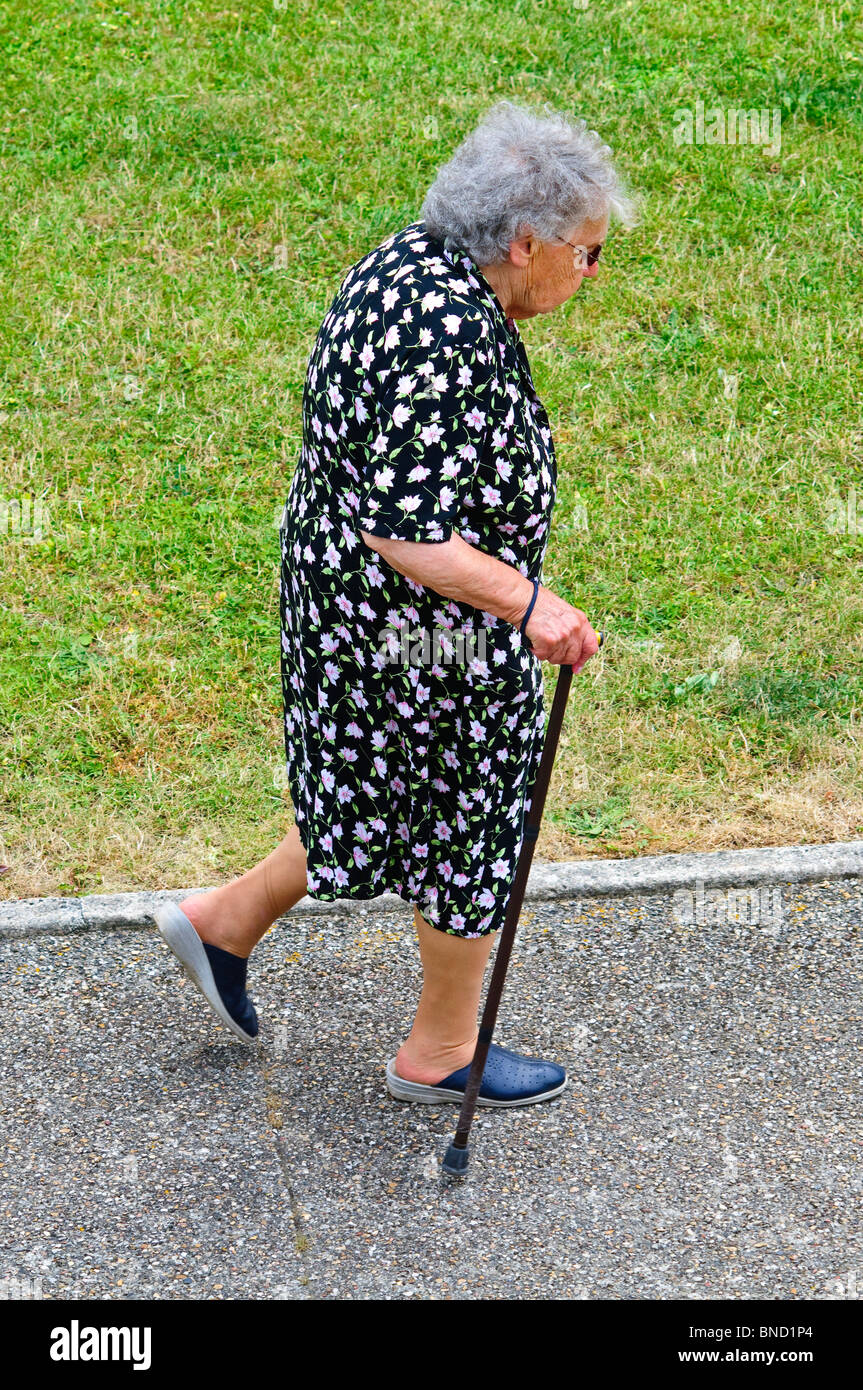 Femme âgée avec bâton de marche marche le long trottoir - France. Banque D'Images